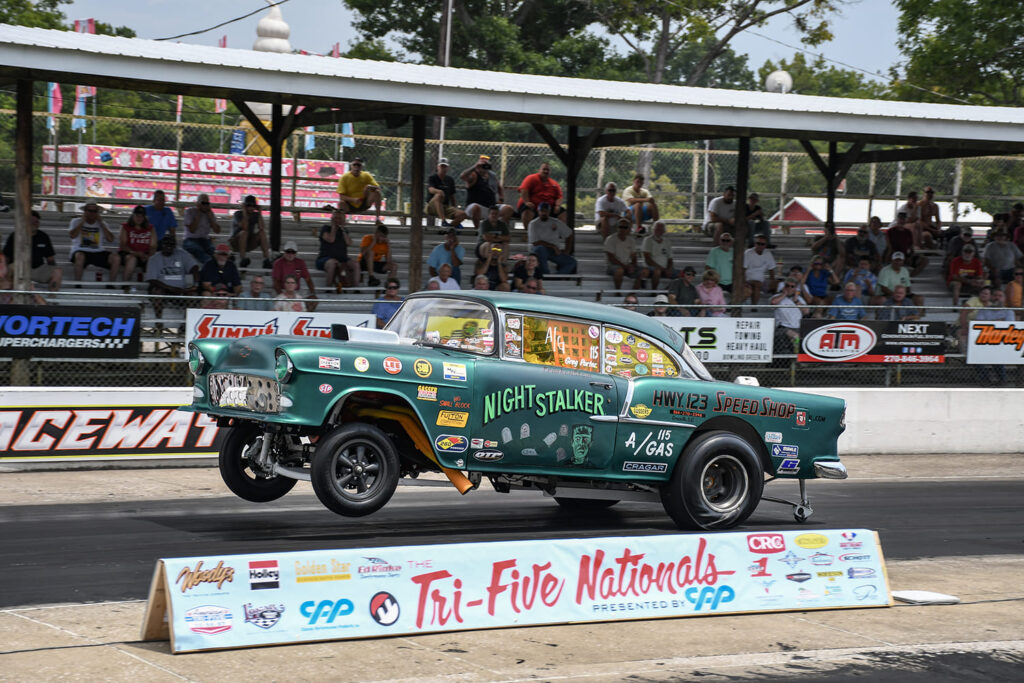 Metallic teal 1955 Chevrolet gasser drag car pulling a high wheelstand off the starting line at Beech Bend Raceway during the Tri-Five Nationals.