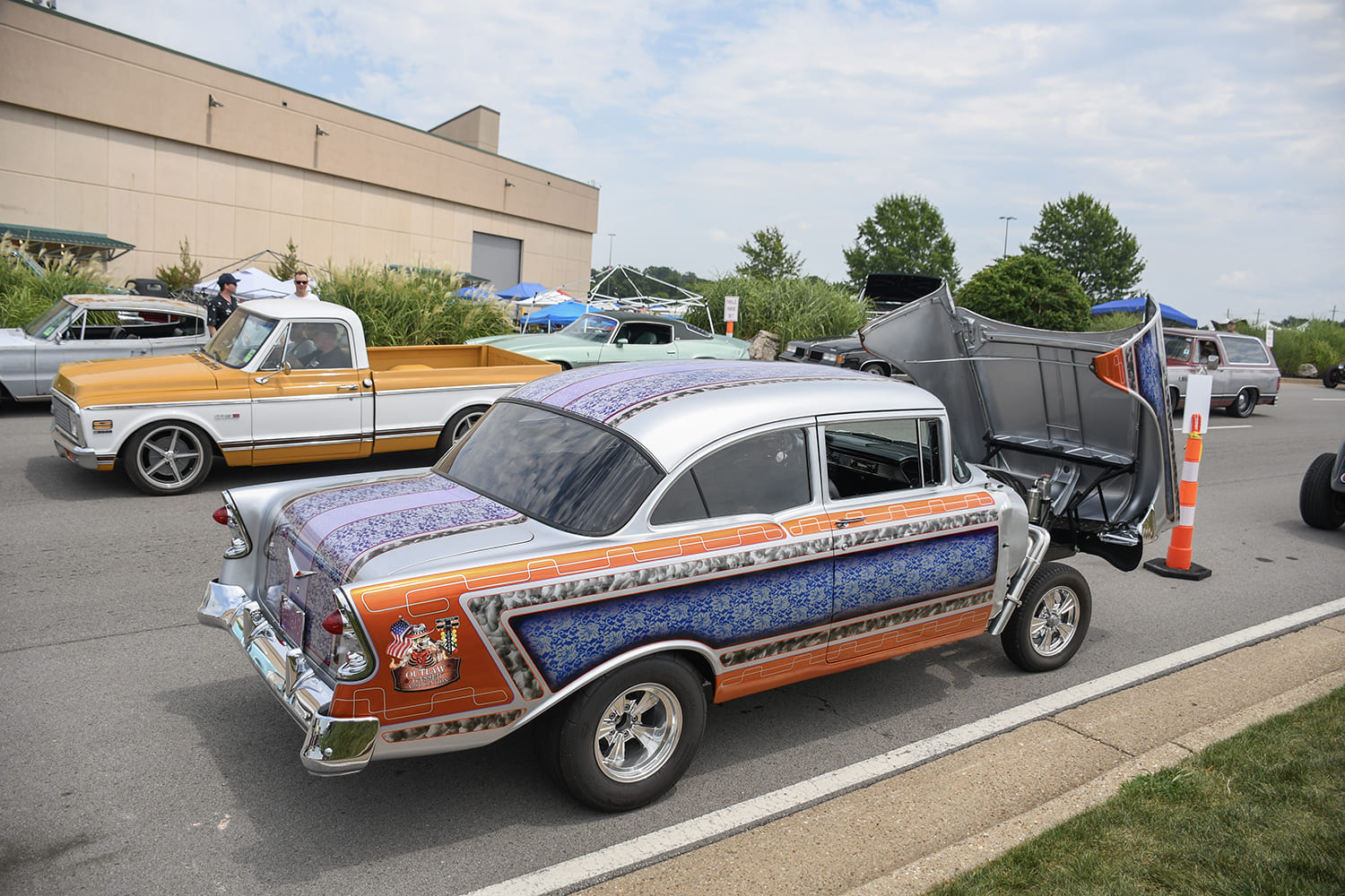 Rear three-quarter view of a custom 1955 Chevrolet gasser featuring intricate multi-pattern lace panel paint, chrome wheels, and an open front tilt front-end.
