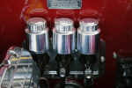 Extreme close-up of three polished billet aluminum brake and clutch master cylinder fluid reservoirs mounted cleanly to the firewall of a candy red 1969 Chevy Camaro restomod.