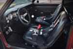 Interior cockpit view of a 1969 Chevy Camaro restomod featuring black vinyl low-back bucket seats with black Simpson racing harnesses, custom white-face gauges, three-spoke steering wheel, and Hurst floor shifter.