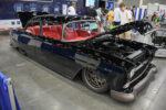 Custom gloss black 1955 Chevrolet restomod with red leather interior, modern bronze wheels, and open hood on display at an indoor car show.