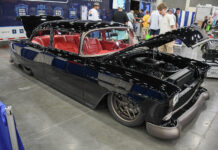 Custom gloss black 1955 Chevrolet restomod with red leather interior, modern bronze wheels, and open hood on display at an indoor car show.