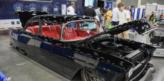Custom gloss black 1955 Chevrolet restomod with red leather interior, modern bronze wheels, and open hood on display at an indoor car show.