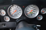 Close-up view of the custom instrument cluster in a 1969 Chevy Camaro featuring silver-faced AutoMeter Pro-Comp Ultra-Lite speedometer, tachometer, and auxiliary gauges with orange needles.