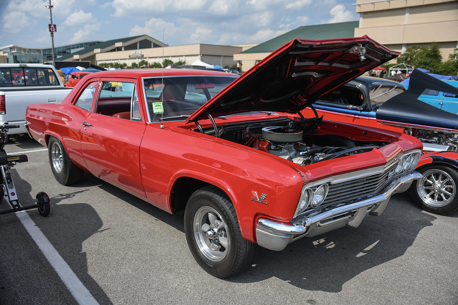 Front three-quarter view of a bright red 1966 Chevrolet Biscayne two-door post car with an open hood showcasing a big-block engine and classic mag wheels.