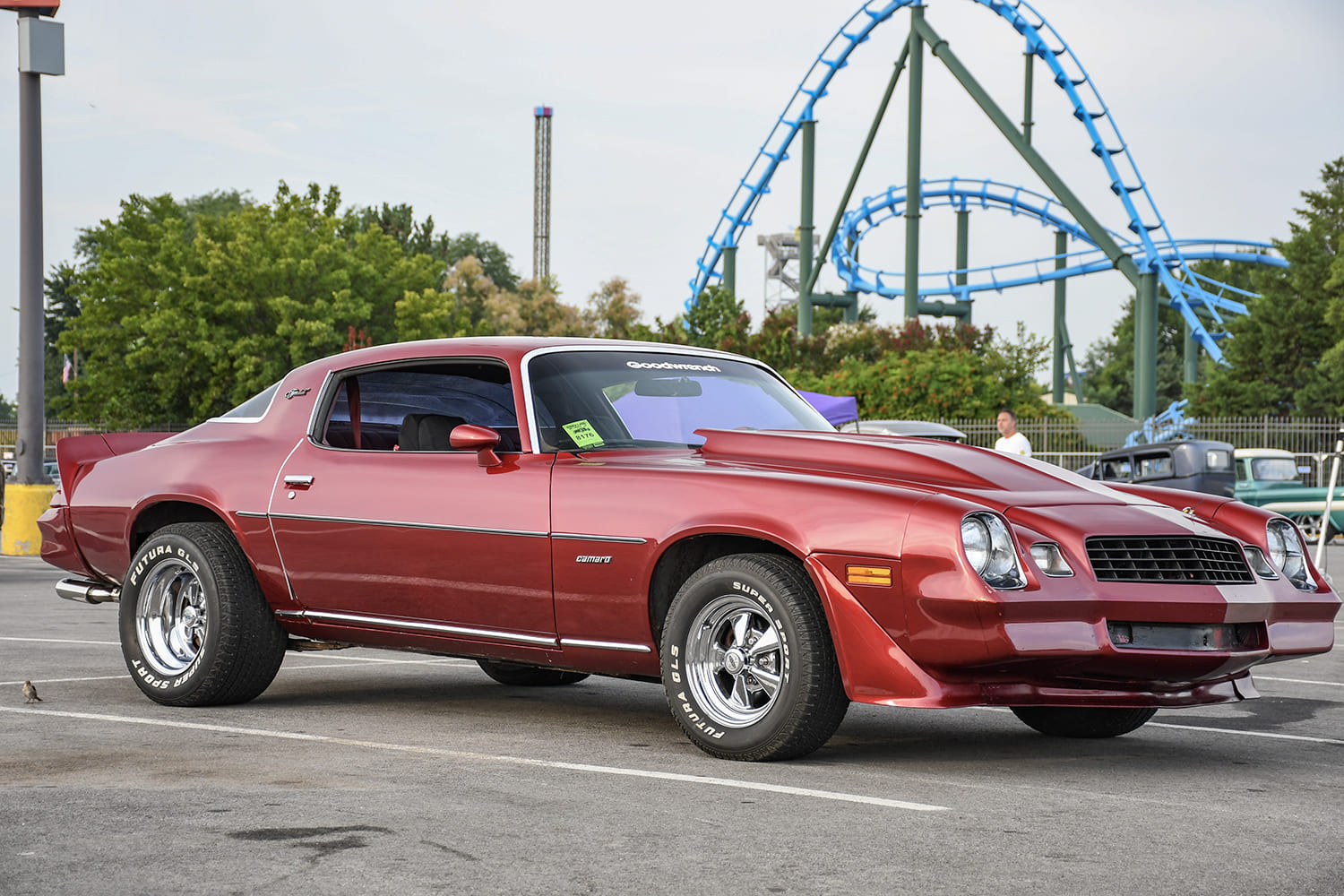 Side three-quarter profile of a metallic maroon late-second-generation Chevrolet Camaro with a large cowl hood and chrome Cragar-style wheels parked in a lot.
