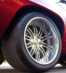 Extreme close-up of the rear wheel on a red 69 Camaro, showcasing a polished deep-dish multi-piece forged wheel wrapped in wide Nitto NT555R performance tires with Wilwood disc brakes behind it.