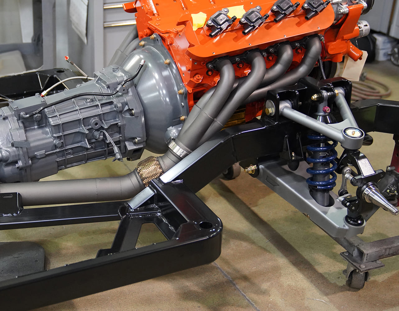 1970 Chevrolet Chevelle Orange engine block with silver headers and black transmission undergoing restoration showcasing custom exhaust components