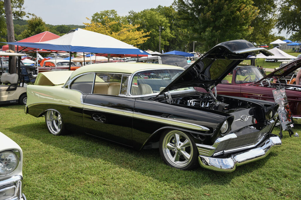 Front three-quarter low angle of a custom black and cream 1956 Chevrolet Bel Air hardtop with an open hood, chrome bumper, and five-spoke billet wheels on the show field.