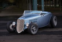 Front three-quarter studio-style shot of an open-wheel metallic light blue 1933 Ford roadster street rod with Halibrand-style wheels and exposed front suspension.