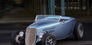 Front three-quarter studio-style shot of an open-wheel metallic light blue 1933 Ford roadster street rod with Halibrand-style wheels and exposed front suspension.