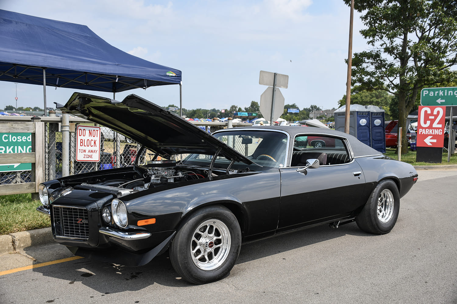 Front three-quarter view of a black split-bumper second-gen Chevy Camaro RS with an open hood, chrome wheels, and wide rear tires parked outside.