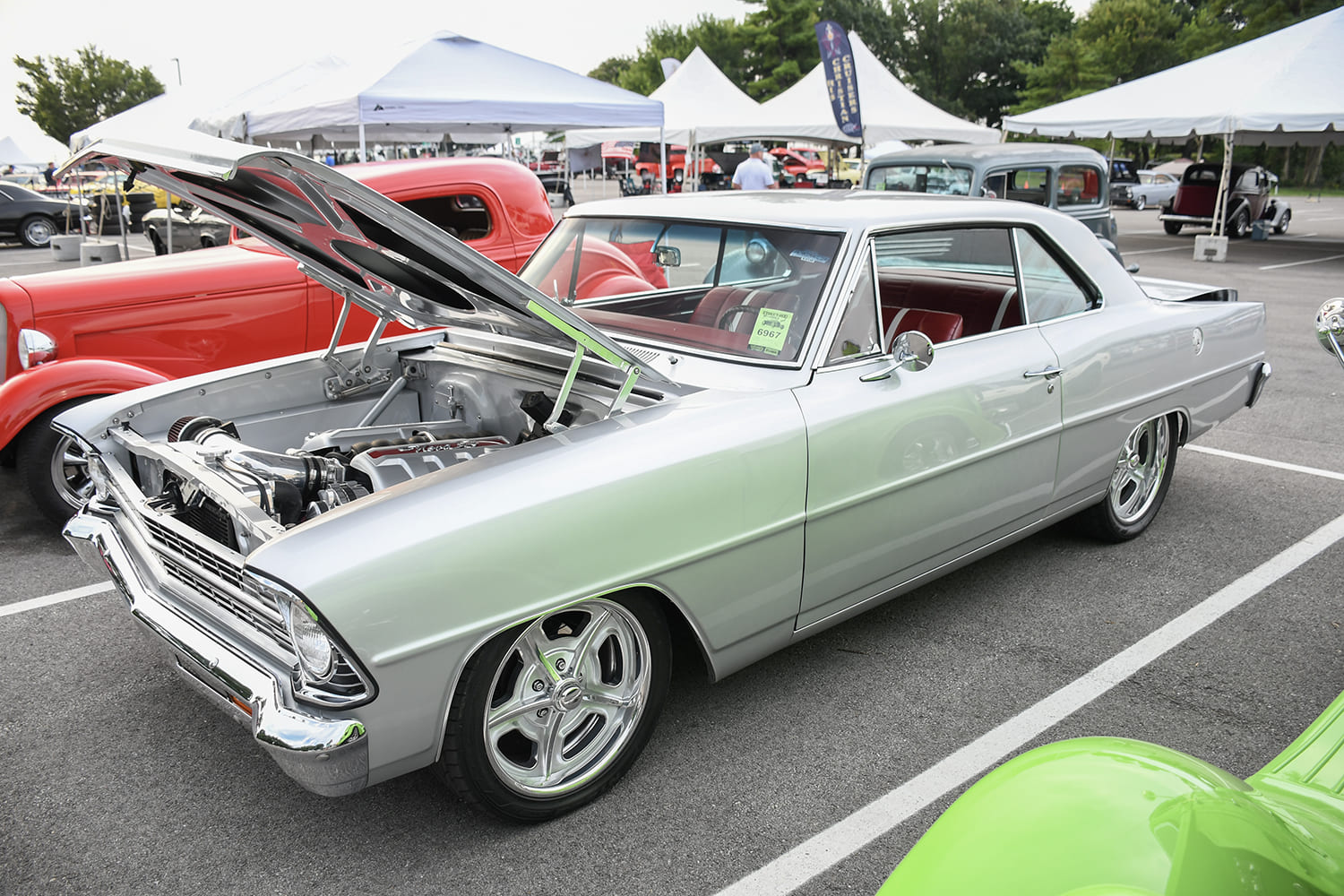 Front quarter view of a metallic silver 1966–1967 Chevrolet Chevy II Nova with an open hood showcasing an LS engine swap, red interior, and chrome billet wheels.