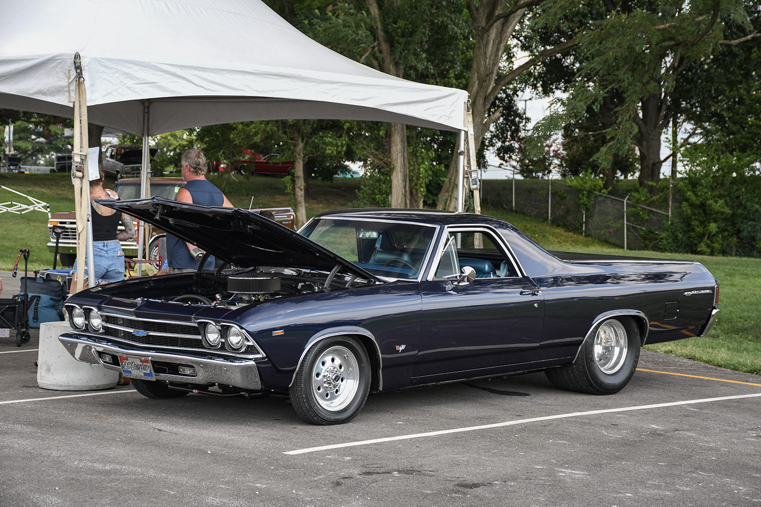 Front three-quarter view of a dark metallic blue 1969 Chevrolet El Camino with an open hood, drag wheels, and wide rear tires.