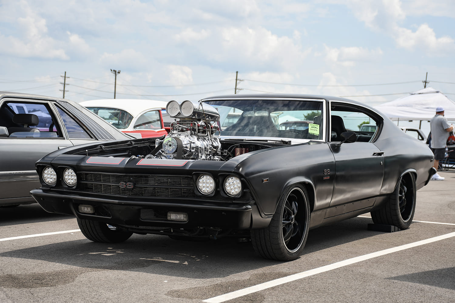 Front three-quarter view of a sinister matte black 1968 Chevy Chevelle SS featuring an exposed chrome supercharger, dual-port scoop, and modern LED headlights.