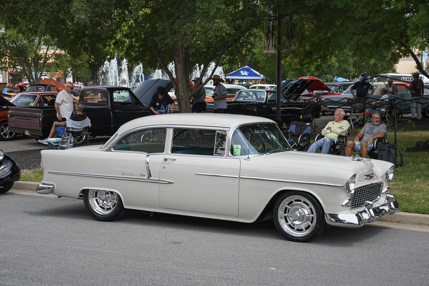 Side three-quarter profile of an off-white 1955 Chevrolet Bel Air hardtop restomod with chrome smoothie-style wheels parked on the street.