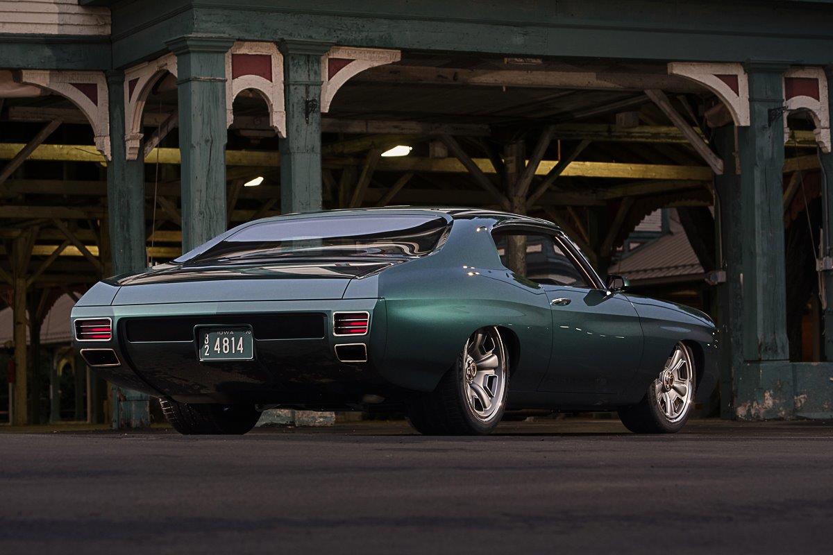 Rear three-quarter view of a low-slung metallic dark green 1970 Chevrolet Chevelle restomod parked inside an open-air vintage train station pavilion.