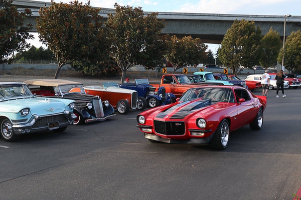 Front three-quarter view of a bright red second-gen Chevrolet Camaro RS parked in a lineup alongside vintage hot rods and classic cars at the Goodguys Pleasanton West Coast Nationals.