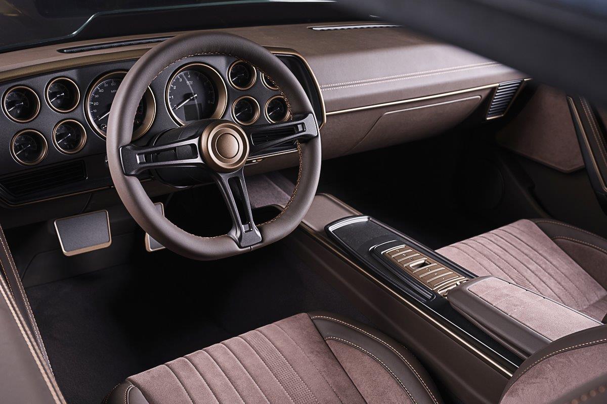 Close-up of a high-end custom brown leather and suede interior featuring vintage-style gauges, a bespoke steering wheel, and a modern center console.