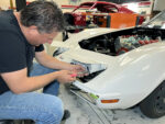 Mechanic adjusting and installing the pop-up headlight housing on a white C3 Chevrolet Corvette during a front-end restoration.