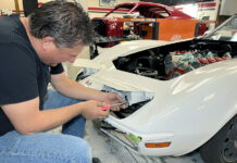 C3 Corvette Headlight Conversion – Going Electric Mechanic adjusting and installing the pop-up headlight housing on a white C3 Chevrolet Corvette during a front-end restoration.