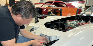 Mechanic adjusting and installing the pop-up headlight housing on a white C3 Chevrolet Corvette during a front-end restoration.