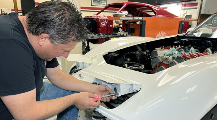 C3 Corvette Headlight Conversion – Going Electric Mechanic adjusting and installing the pop-up headlight housing on a white C3 Chevrolet Corvette during a front-end restoration.
