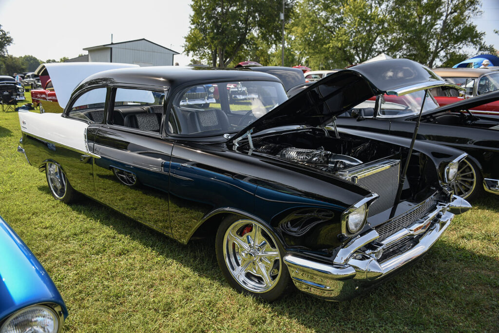 Front three-quarter view of a custom black and white 1957 Chevrolet Bel Air hardtop with an open hood displaying a supercharged engine and polished five-spoke wheels.