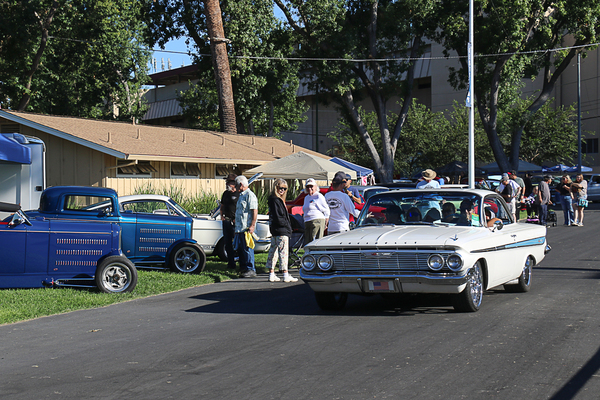 Front three-quarter view of a white 1960 Chevrolet Impala hardtop cruising down the fairgrounds lane past parked hot rods at the Goodguys Pleasanton West Coast Nationals.
