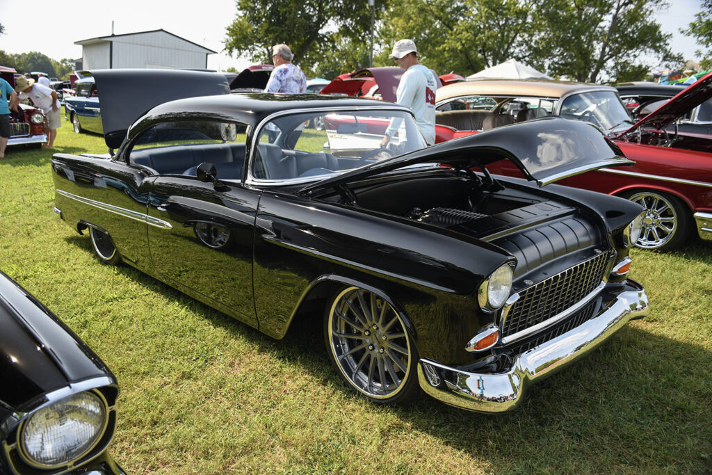 Front three-quarter view of a slammed black 1955 Chevrolet Bel Air hardtop featuring modern multi-spoke wheels and a custom detailed engine bay.