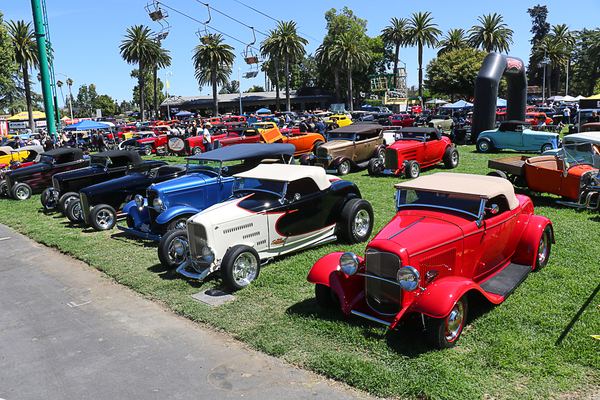 High-angle view of a lineup of red, white, blue, and black 1932 Ford roadsters parked on the lawn under palm trees at the Goodguys Pleasanton West Coast Nationals.