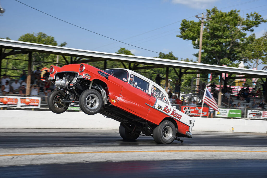 Red and white 1955 Chevrolet gasser "Red Baron" pulling a high wheelstand launch down the drag strip during the Tri-Five Nationals.