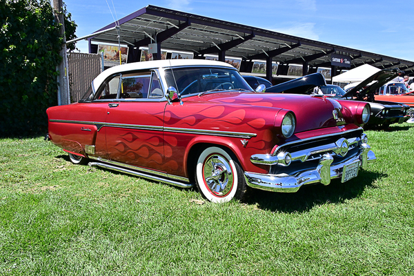 Front three-quarter view of a custom red 1954 Ford Crestline Victoria hardtop with custom flame paint and whitewall tires at the Goodguys Pleasanton West Coast Nationals.