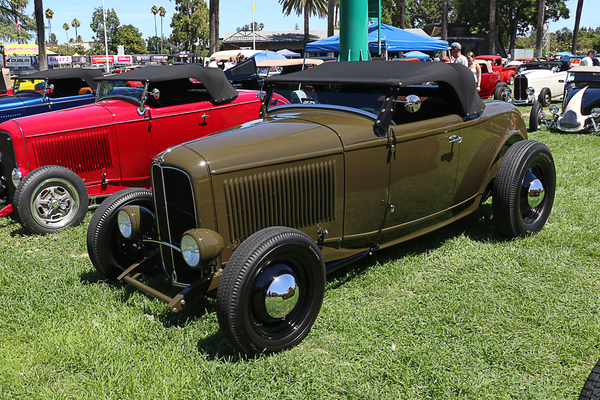 Front three-quarter view of an olive green 1932 Ford roadster hot rod with black steel wheels and chrome hubcaps parked on the grass at the Goodguys Pleasanton West Coast Nationals.