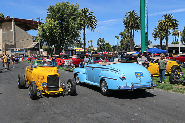 Rear three-quarter view of a sky blue 1946–1948 Ford convertible driving alongside a bright yellow 1932 Ford roadster hot rod at the Goodguys Pleasanton West Coast Nationals.