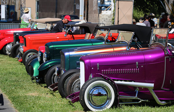 Side view lineup of traditional hot rods leading with a metallic magenta purple 1932 Ford roadster with white wall tires parked on the grass at the Goodguys Pleasanton West Coast Nationals.