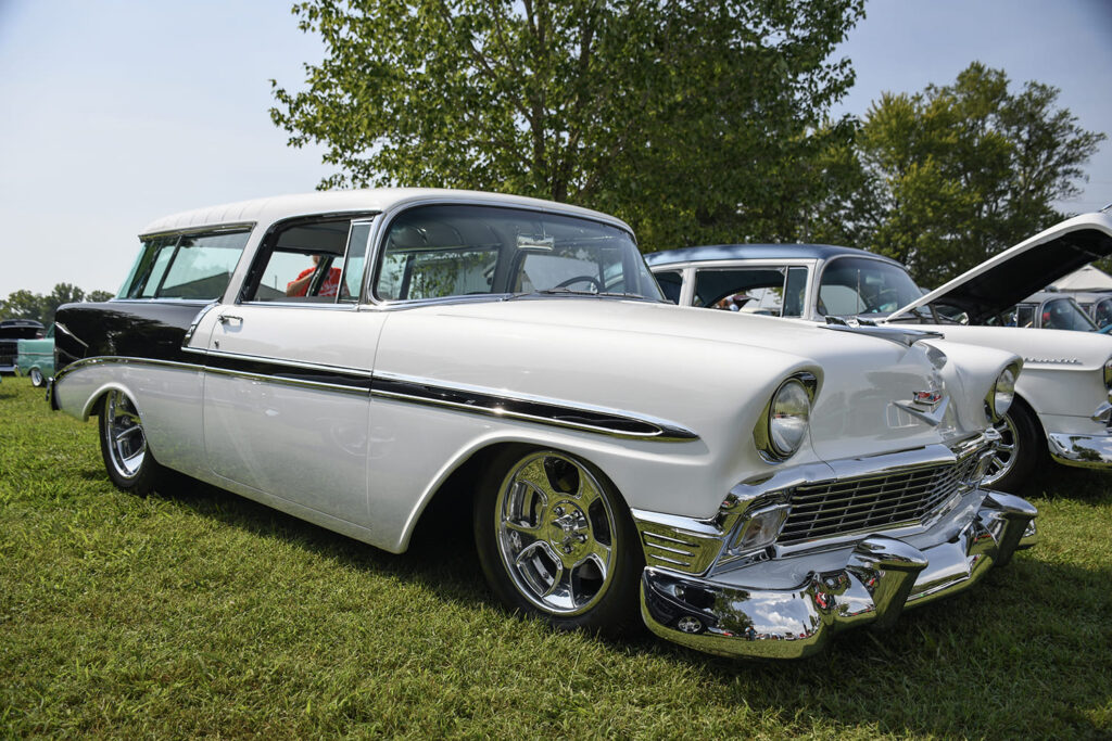 Front three-quarter view of a lowered white and black 1956 Chevrolet Nomad wagon with "ET Mag" style wheels parked on the grass.