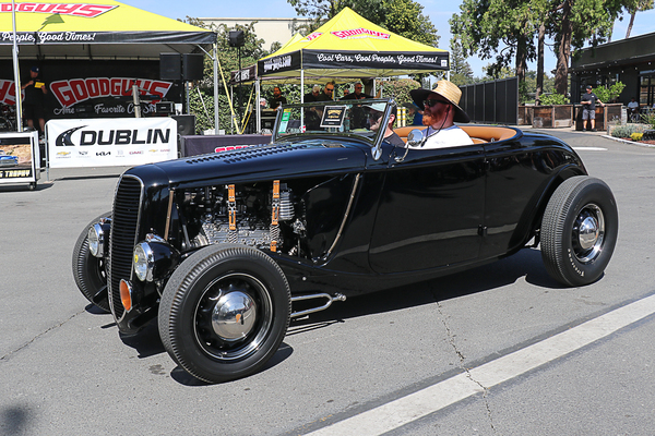Front three-quarter view of an open-wheel gloss black 1933–1934 Ford roadster hot rod cruising past the Goodguys tent at the Goodguys Pleasanton West Coast Nationals.