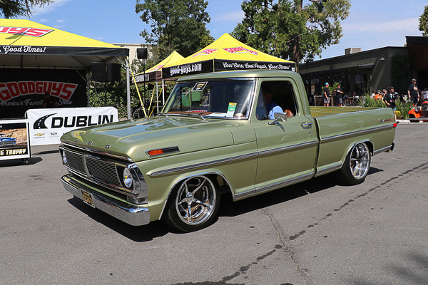 Front three-quarter view of a lowered metallic light olive green 1970–1972 Ford F-100 Ranger pickup truck driving past the Goodguys tent at the Goodguys Pleasanton West Coast Nationals.