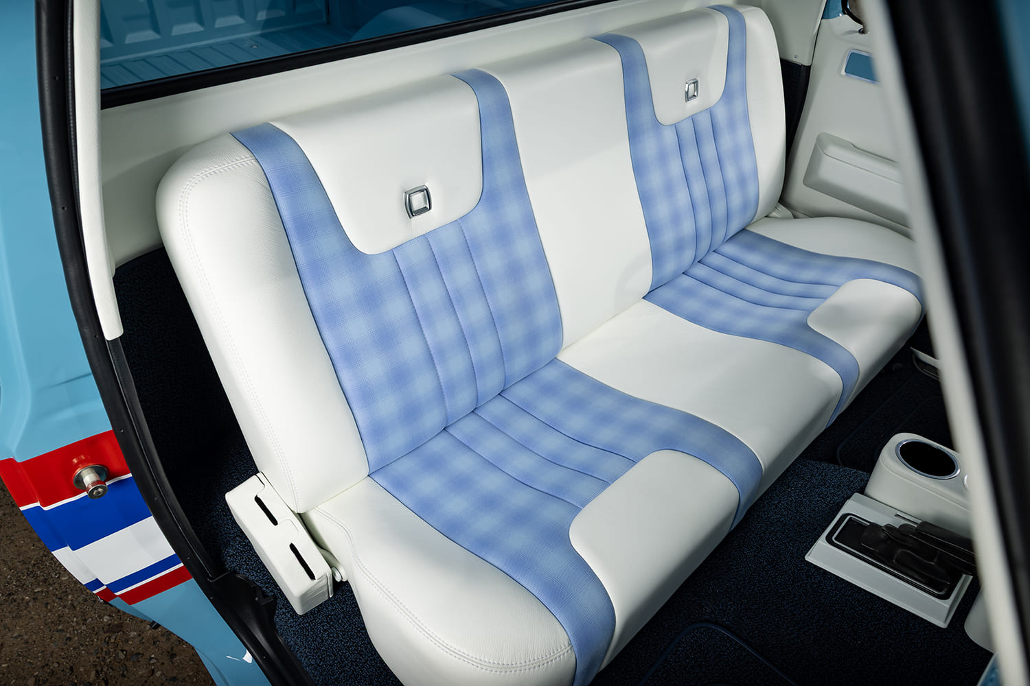 Custom interior of a 1976 Chevy k10 pickup truck showing a white vinyl bench seat with blue plaid inserts and blue carpet.