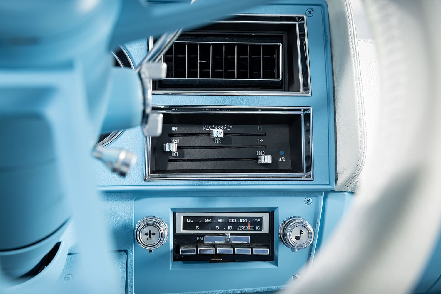 Close-up detail of the center dashboard in a restored light blue 1976 Chevy truck showing the Vintage Air slider climate controls, A/C vent, and retro-style push-button radio.