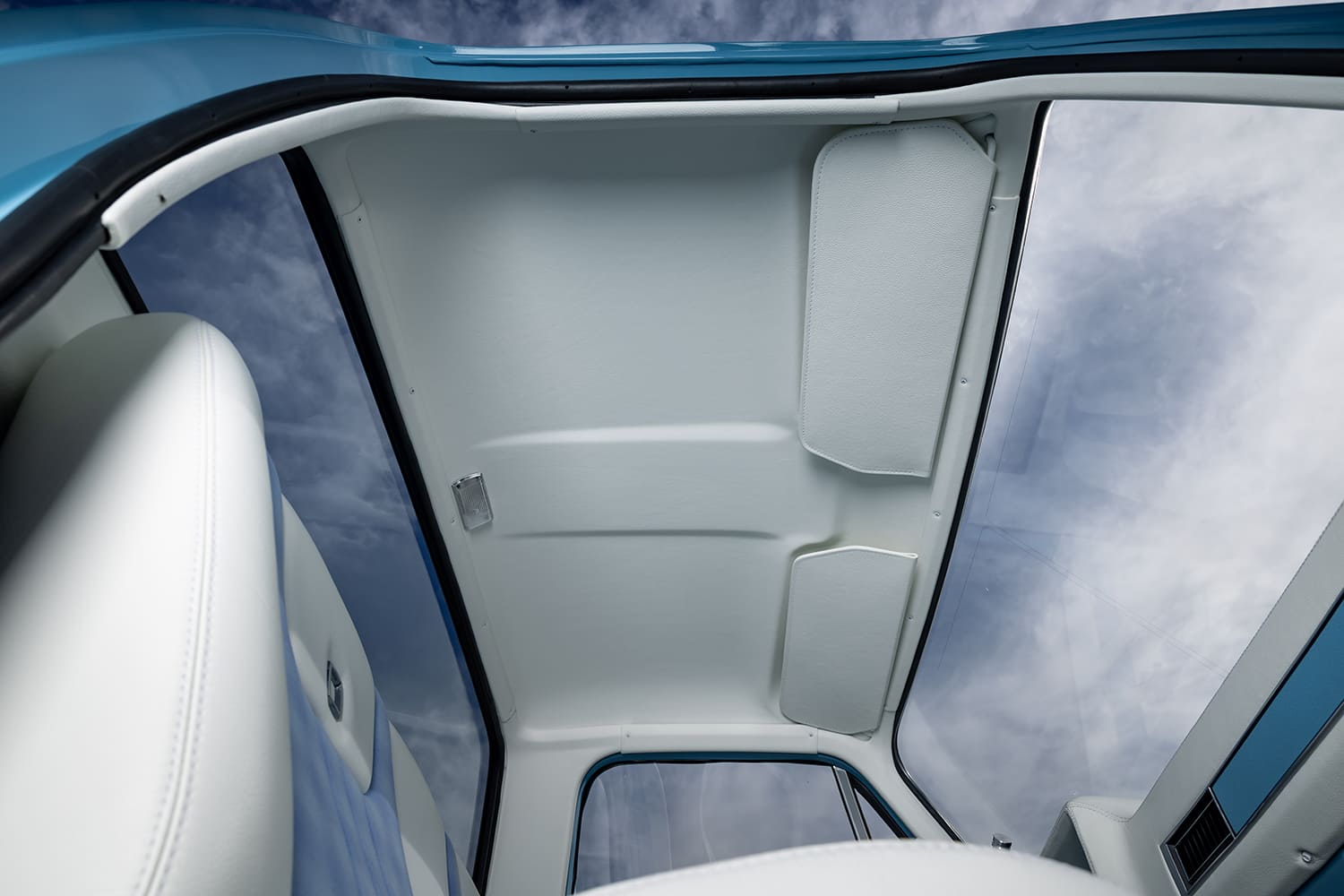 Low-angle interior view of a restored 1976 Chevy truck cab featuring a clean custom white leather headliner, matching stitched sun visors, and a dome light.