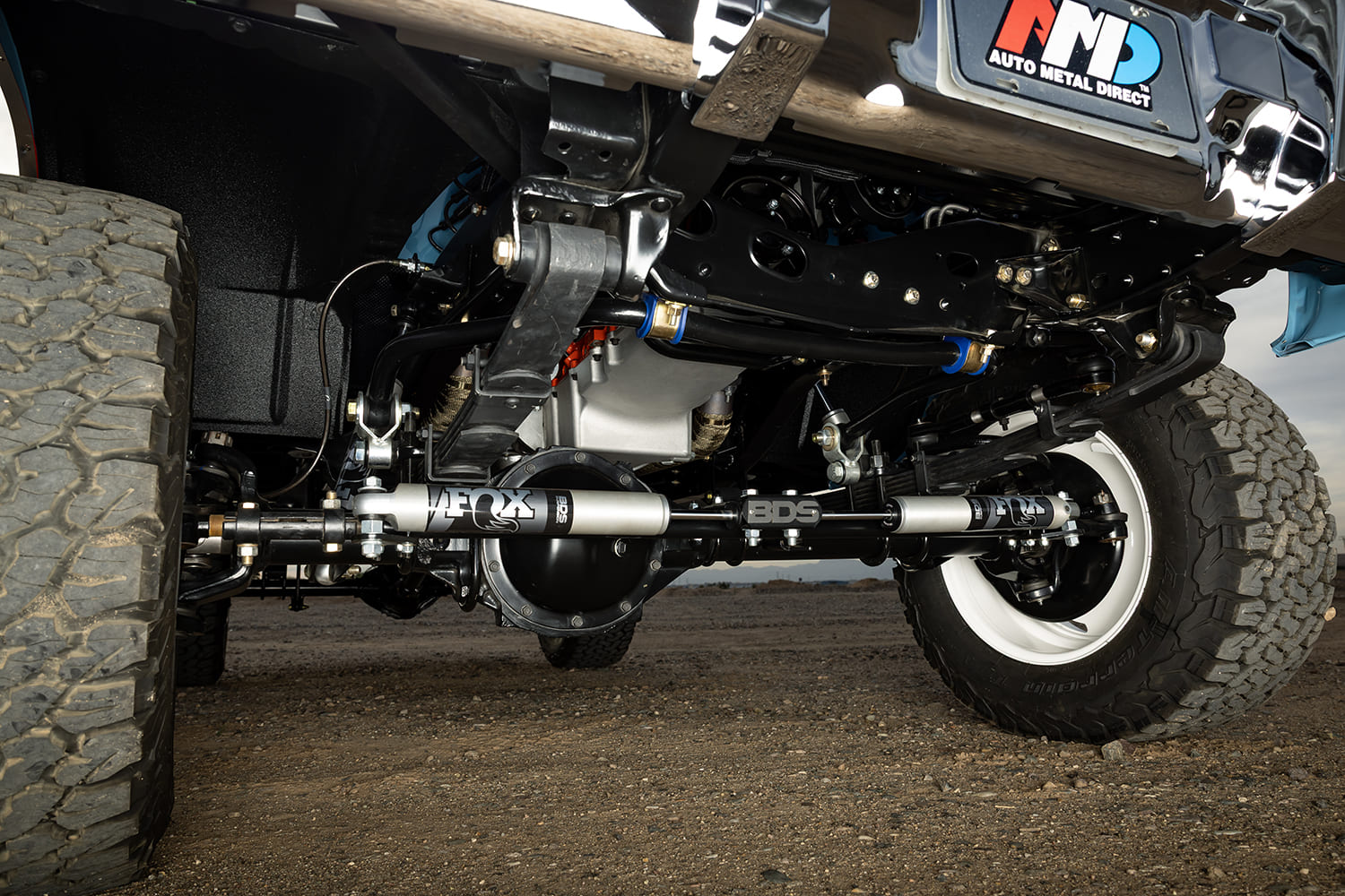 Underside view of a restored 1976 Chevy 4x4 truck showing the front axle, leaf springs, and a BDS dual steering stabilizer setup with Fox shocks