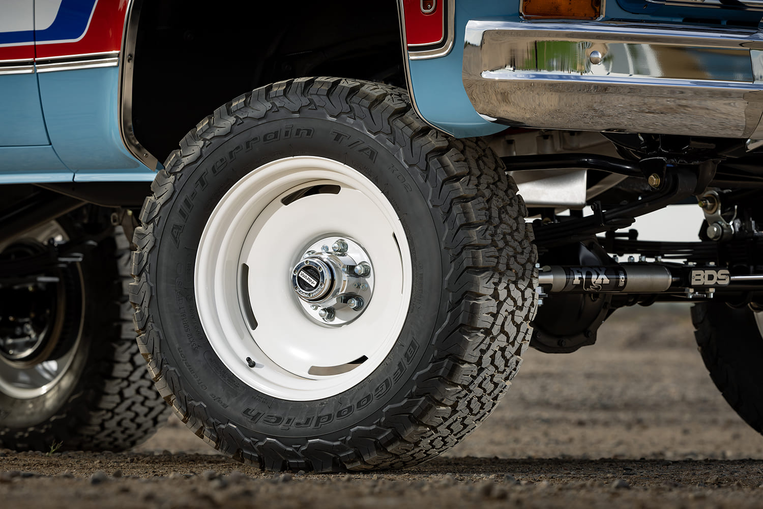 Close-up of a lifted 1976 Chevy truck's front wheel featuring a classic white steelie-style rim, Warn locking hub, and BFGoodrich All-Terrain T/A KO2 off-road tire.