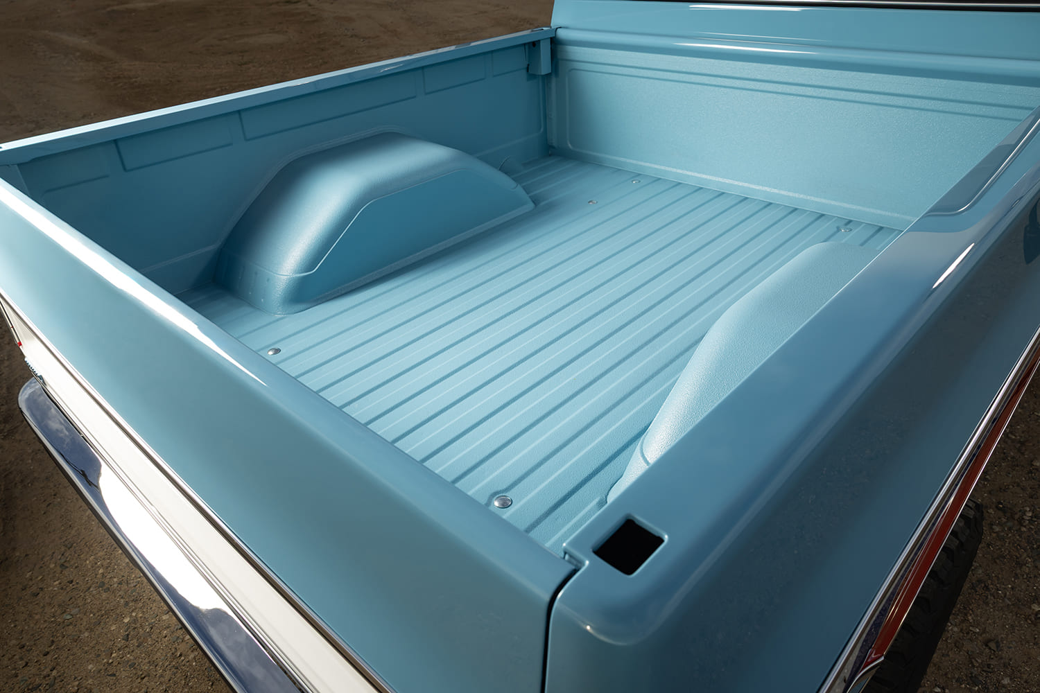 Overhead view looking into the clean truck bed of a restored light blue 1976 Chevy pickup, featuring a seamless color-matched spray-in bedliner and chrome accents.