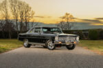 Front three-quarter angle of a glossy black 1966 Chevrolet Nova Super Sport restomod with chrome wheels parked on an asphalt road at sunset.