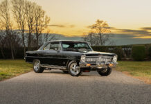 Front three-quarter angle of a glossy black 1966 Chevrolet Nova Super Sport restomod with chrome wheels parked on an asphalt road at sunset.