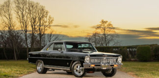 Front three-quarter angle of a glossy black 1966 Chevrolet Nova Super Sport restomod with chrome wheels parked on an asphalt road at sunset.