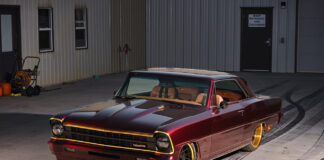 Custom 1967 Chevrolet Chevy II Nova restomod in deep candy apple red paint with gold accents and custom wheels parked outside a workshop.
