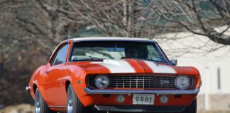 Low-angle front shot of an original Hugger Orange 1969 Chevrolet Camaro Z/28 with white racing stripes, cowl induction hood, and USA-1 front novelty plate on asphalt.